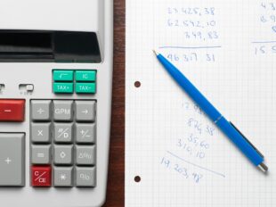 calculator next to paper with numbers written on and a pen 