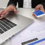 close-up of hands using computer keyboard and smartphone