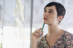 woman holding a pen under her chin and looking at notices