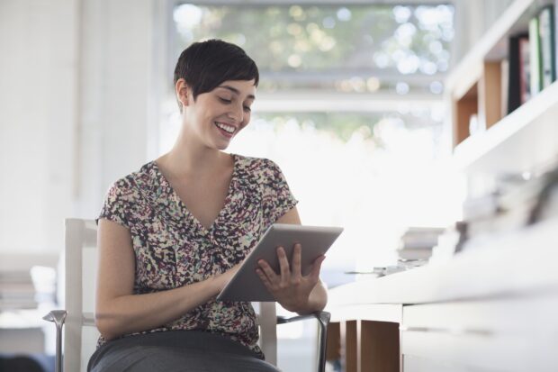 Woman sitting in a chair, smiling and working on a tablet device