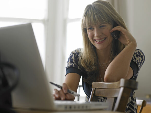 smiling lady talking on a mobile phone looking at a laptop