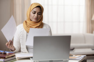 Female office worker looking through papers, working at her laptop