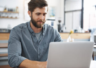 Smiling man, sitting in a cafe using a laptop