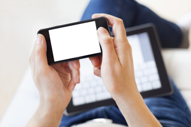 man holding a mobile phone with a tablet device on his knee