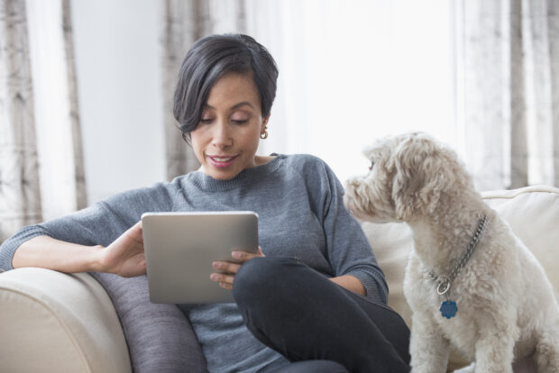 Woman sitting on a sofa, using a digital tablet sitting with a dog