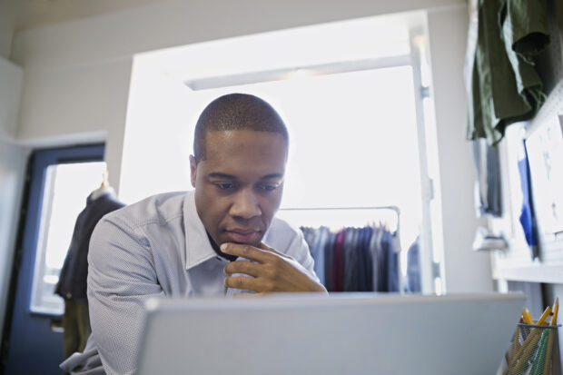 Man sitting in a clothing shop looking at a laptop