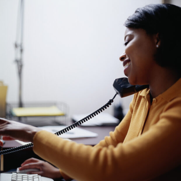 Smiling woman on the phone and working at her computer