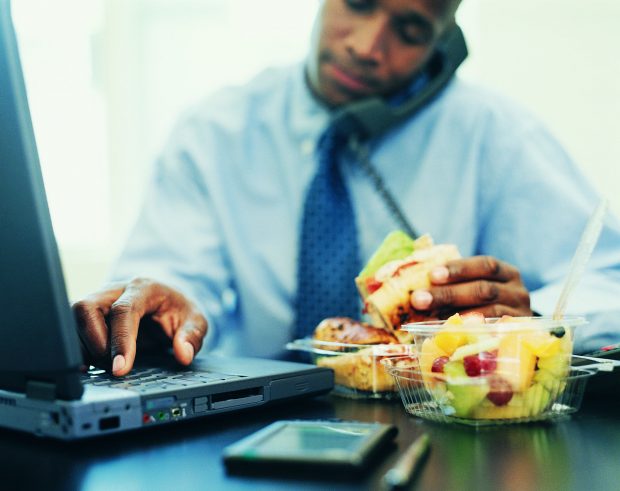 man eating lunch working at a computer and answering the phone